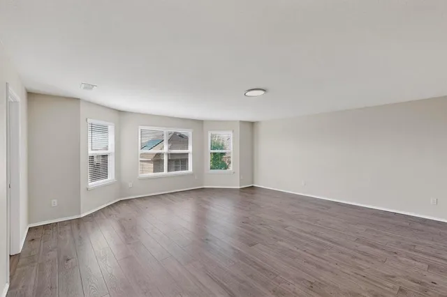 a view of an empty room with wooden floor and windows