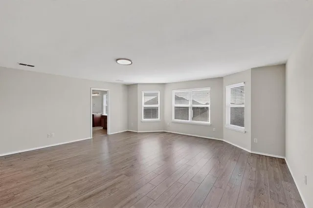 a view of an empty room with wooden floor and windows