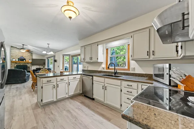 a kitchen with stainless steel appliances granite countertop a sink dishwasher stove and white cabinets with wooden floor