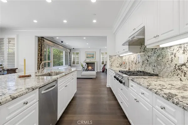 a view of a dining room and livingroom with furniture wooden floor a rug a kitchen view and a chandelier