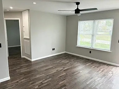 an empty room with wooden floor a ceiling fan and windows