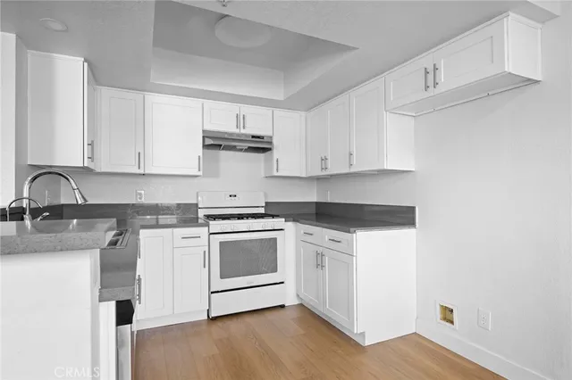 a kitchen with stainless steel appliances granite countertop a sink stove and white cabinets with wooden floor