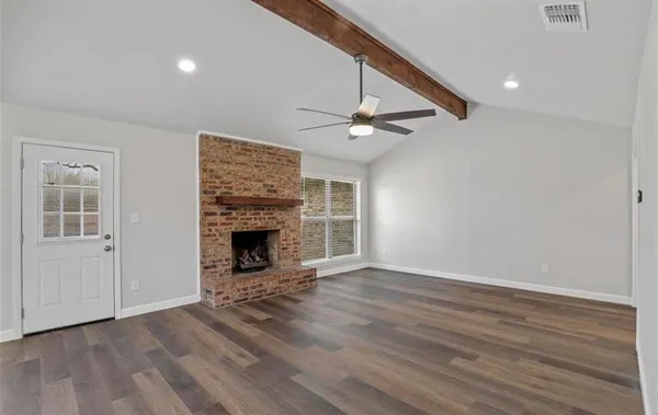 a view of an empty room with wooden floor fireplace and a window