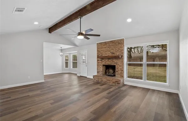 a view of an empty room with wooden floor fireplace and a window