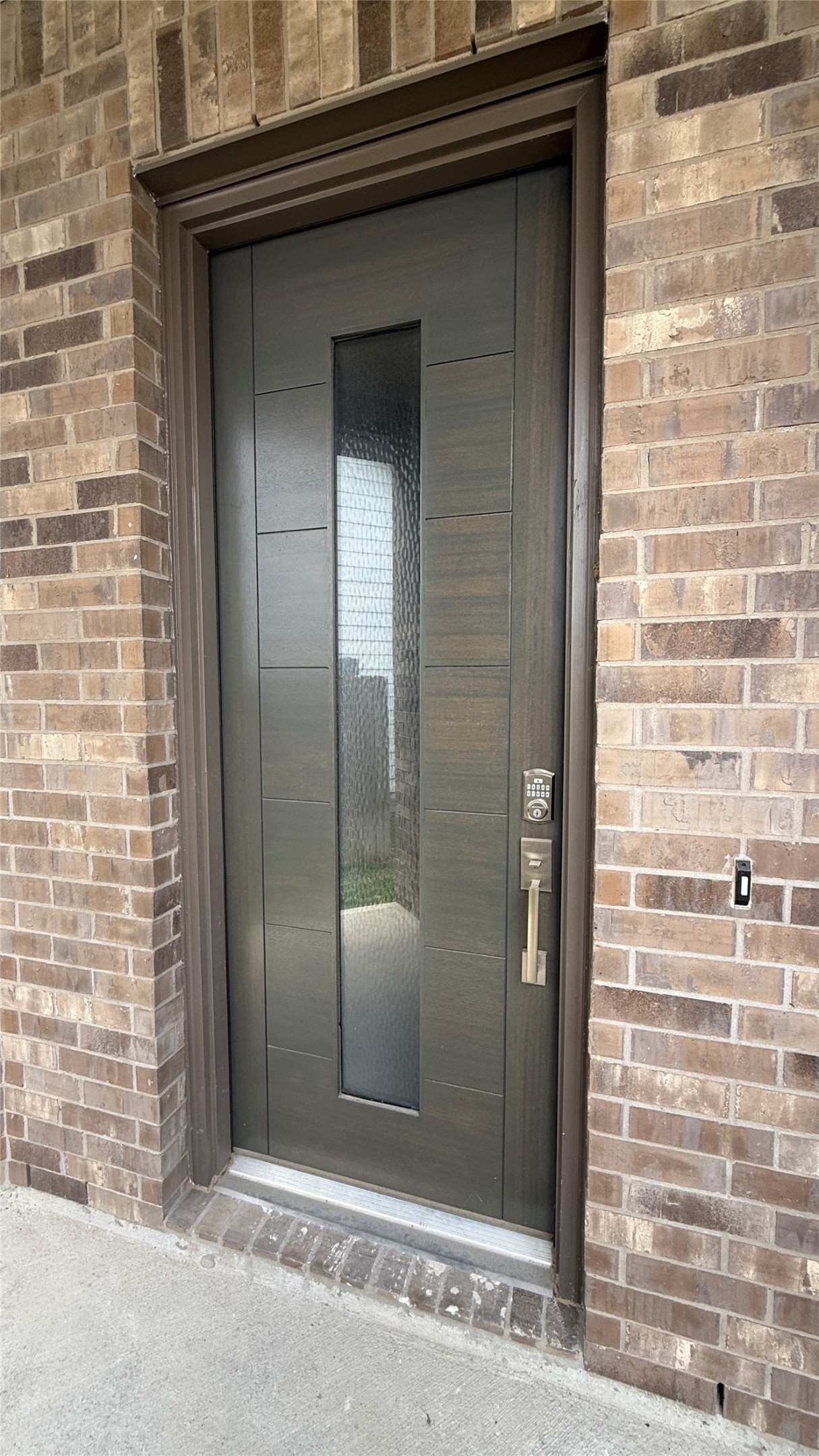 31961 Retama Rnch Drive Spring, TX 77386 - Photo 5 of 25 This photo shows a modern front door with a sleek design, featuring a vertical glass panel and a sturdy handle, set within a brick exterior.