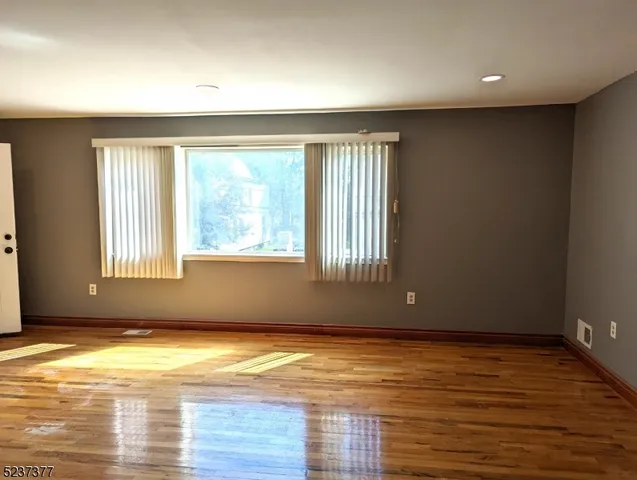 an empty room with wooden floor and windows with curtains
