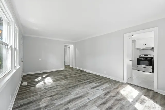 a view of empty room with wooden floor and kitchen