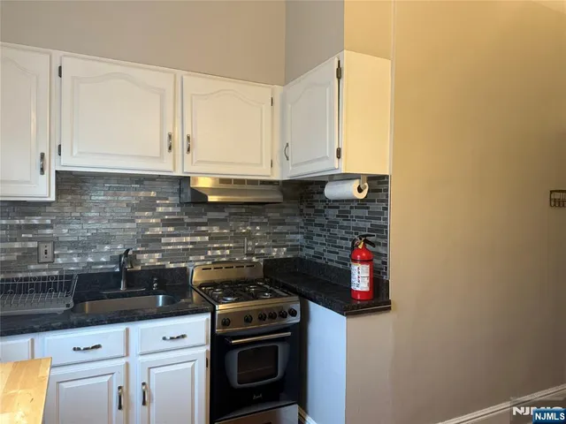 a kitchen with stainless steel appliances granite countertop a stove a sink and white cabinets