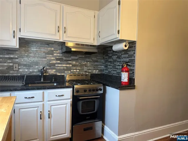 a kitchen with stainless steel appliances granite countertop a stove a sink and white cabinets