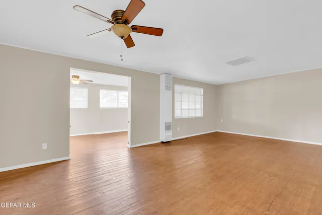 an empty room with wooden floor fan and windows