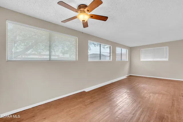 an empty room with wooden floor chandelier fan and windows