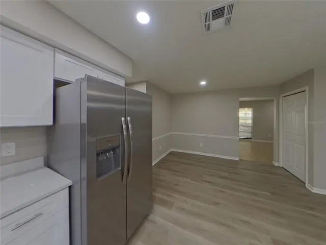 a view of a refrigerator in kitchen and an empty room with wooden floor