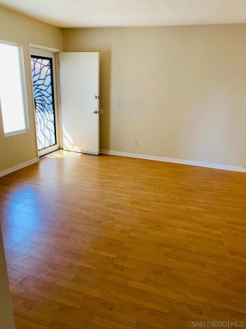 a view of an empty room with wooden floor and a small bathroom