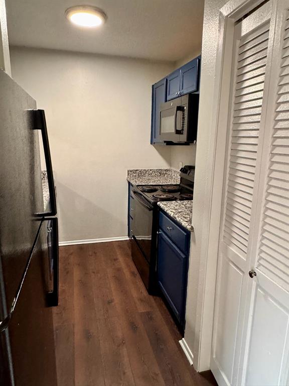 624 East 3rd Street, Unit 207 Springtown, TX 76082 - Photo 2 of 7 Kitchen featuring wood-finish flooring, blue cabinetry, a stainless steel microwave, a black electric range, and a black refrigerator