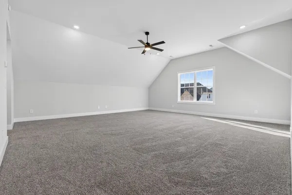 an empty room with a ceiling fan and kitchen view