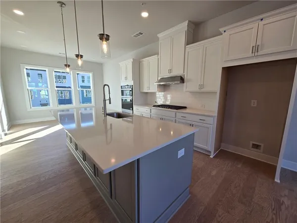 a kitchen with kitchen island granite countertop a stove a sink a refrigerator and white cabinets with wooden floor