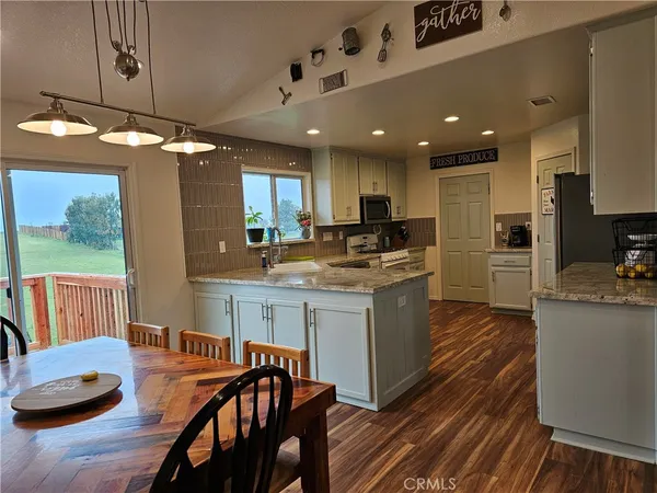 a kitchen with stainless steel appliances granite countertop a stove refrigerator a sink dishwasher and a dining table with wooden floor