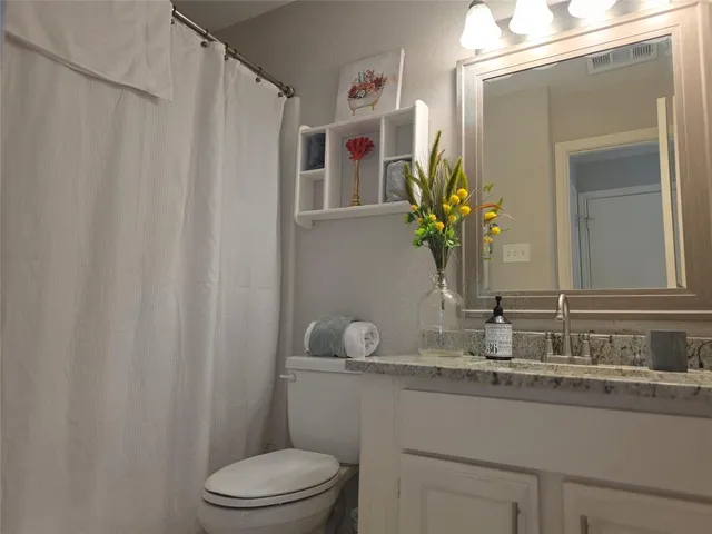 a bathroom with a granite countertop sink vanity mirror and toilet