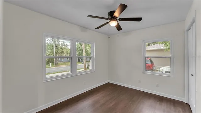 an empty room with wooden floor ceiling fan and windows