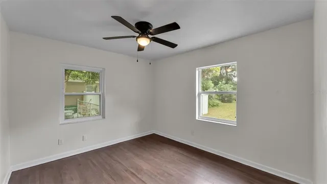 an empty room with wooden floor ceiling fan and windows