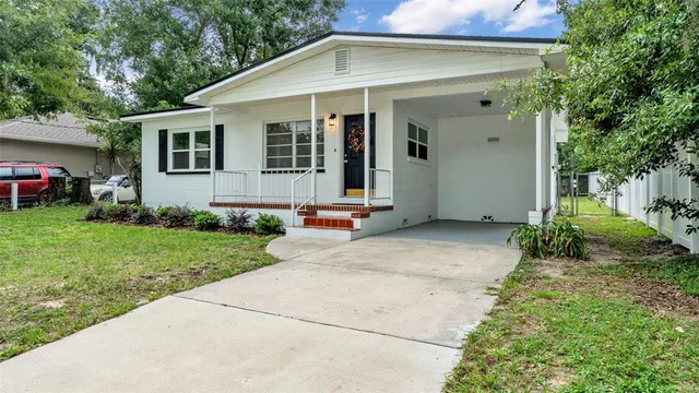 a view of a white house with a small yard plants and a large tree