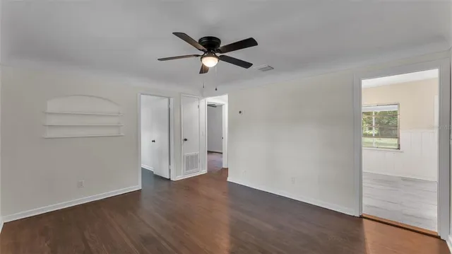 an empty room with wooden floor a ceiling fan and windows