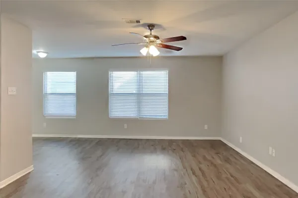 an empty room with wooden floor fan and windows