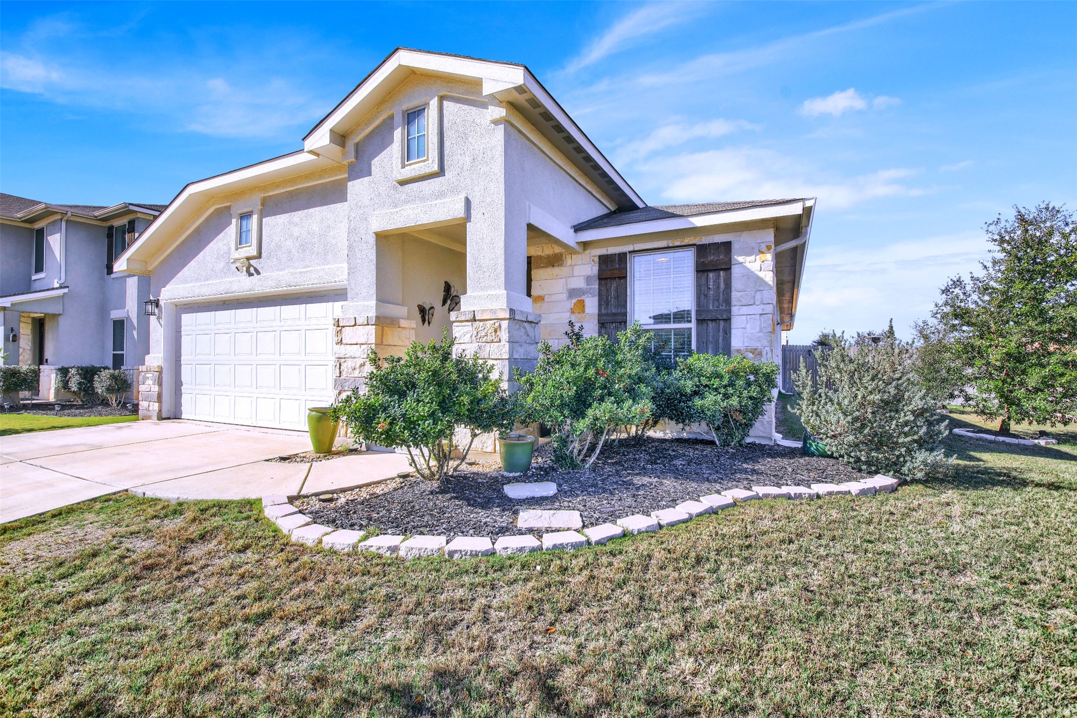 View of front of home with stone siding, a front lawn, driveway, and stucco siding