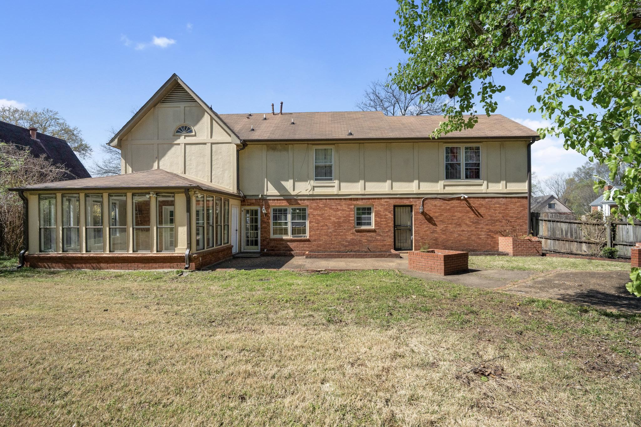 Back of house with a sunroom, a shingled roof, a patio area, board and batten siding, and brick siding