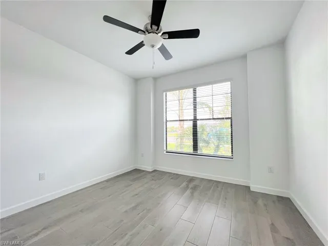 an empty room with wooden floor ceiling fan and windows