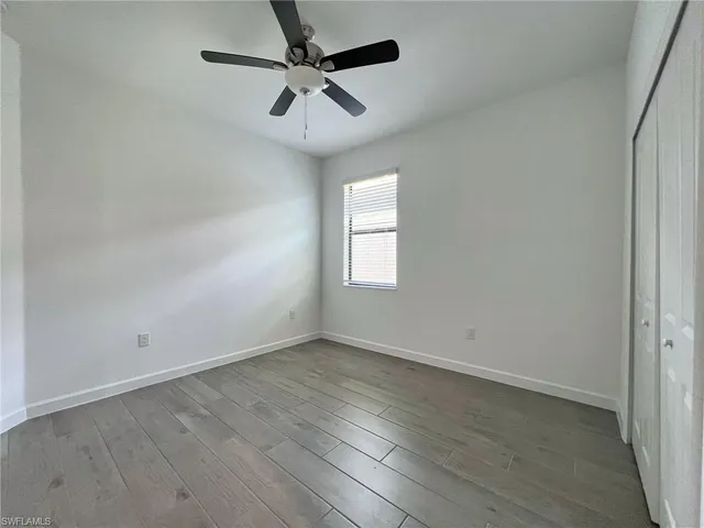 an empty room with wooden floor ceiling fan and windows