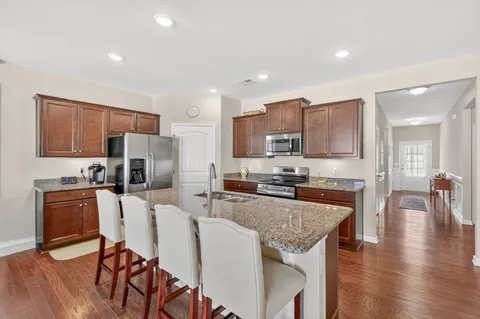 a kitchen with stainless steel appliances granite countertop a stove top oven a sink a refrigerator a dining table and chairs with wooden floor