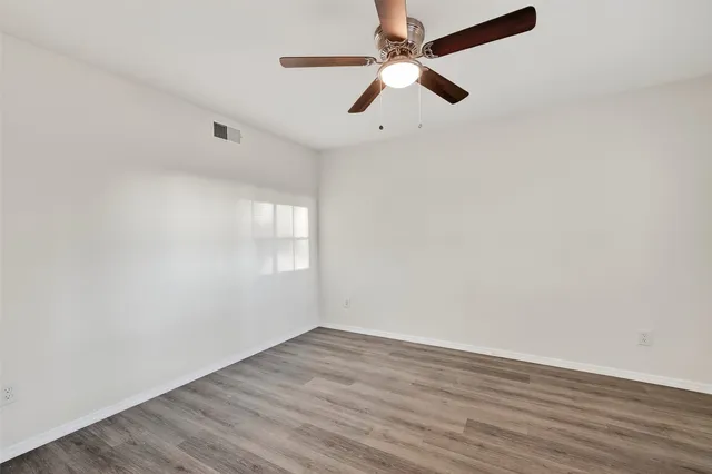 an empty room with wooden floor ceiling fan and window