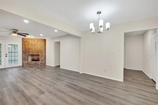 an empty room with wooden floor chandelier and windows