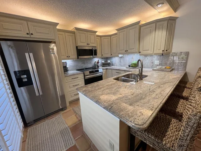 a kitchen with granite countertop a refrigerator a stove a sink a kitchen island and cabinets