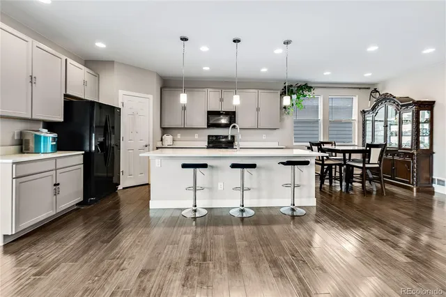 a kitchen with stainless steel appliances kitchen island granite countertop a stove a sink a refrigerator and a dining table with wooden floor