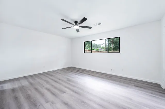 an empty room with wooden floor fan and windows