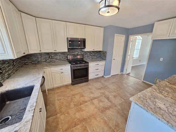 a kitchen with granite countertop a sink a stove top oven and cabinetry