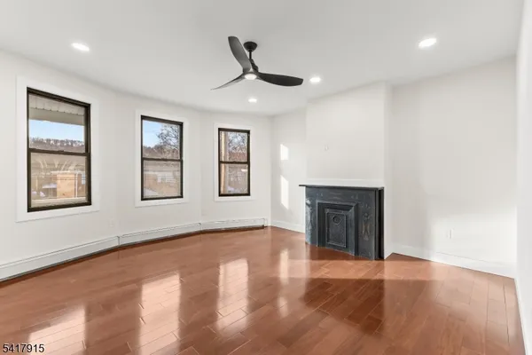 an empty room with wooden floor a ceiling fan and a kitchen view