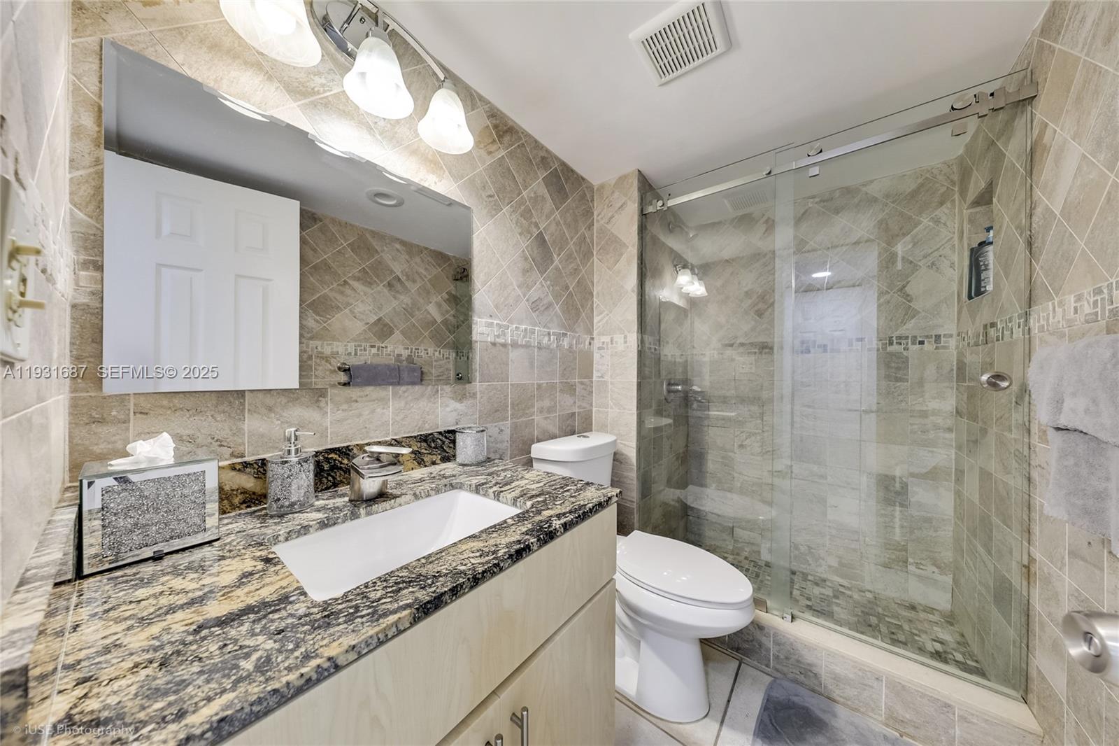 4301 Collins Avenue, Unit 803 Miami Beach, FL 33140 - Photo 21 of 25 a bathroom with a granite countertop sink a toilet a mirror and shower
