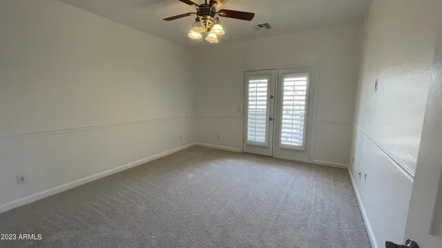 an empty room with a chandelier fan and windows