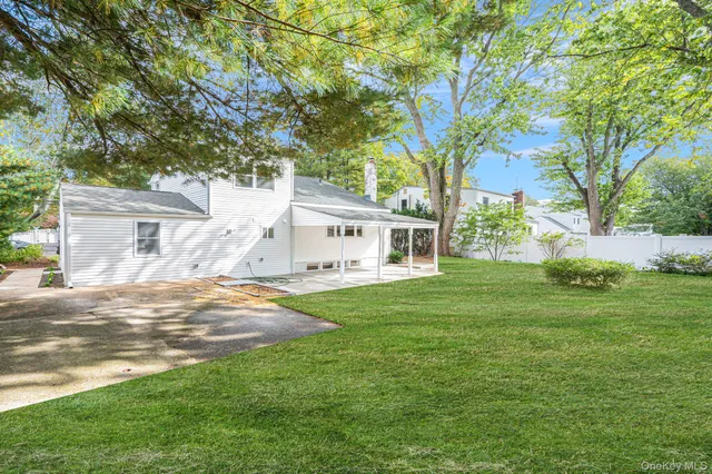 a view of a white house in front of a big yard with large trees