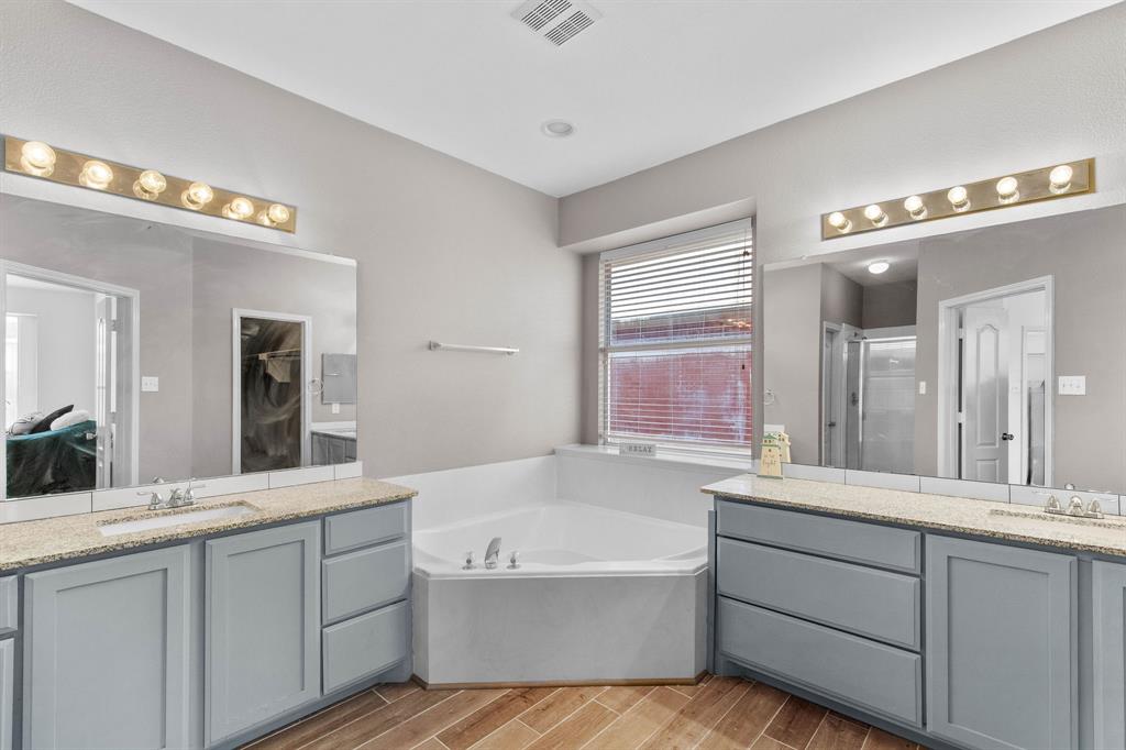 2700 Hereford Road Denton, TX 76210 - Photo 17 of 36 Bathroom featuring a corner soaking tub with deck, dual vanities with light-colored countertops, large mirrors with overhead strip lighting, and wood-finish flooring