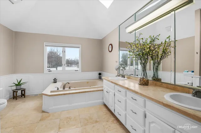 a spacious bathroom with a double vanity sink a large mirror a bathtub and next to a window