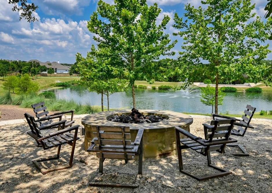 1208 Sweetspire Street Leander, TX 78641 - Photo 33 of 36 Stone fire pit area with gravel groundcover, surrounded by mature trees, overlooking a serene pond with a fountain feature