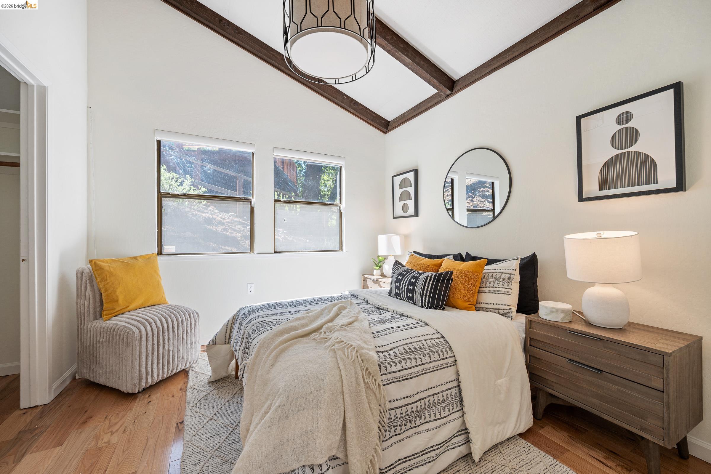 6600 Heather Ridge Way Oakland, CA 94611 - Photo 28 of 66 Vaulted ceiling with exposed wood beams, wood-finish flooring, two large windows, white walls, and a contemporary ceiling light fixture