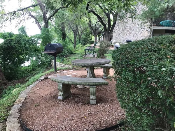 a view of a backyard with table and chairs potted plants and large trees