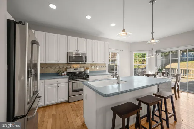 a kitchen with stainless steel appliances granite countertop a dining table chairs refrigerator and microwave