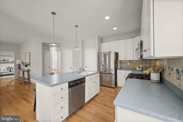 a kitchen with stainless steel appliances granite countertop a stove a sink a microwave a refrigerator and white cabinets with wooden floor