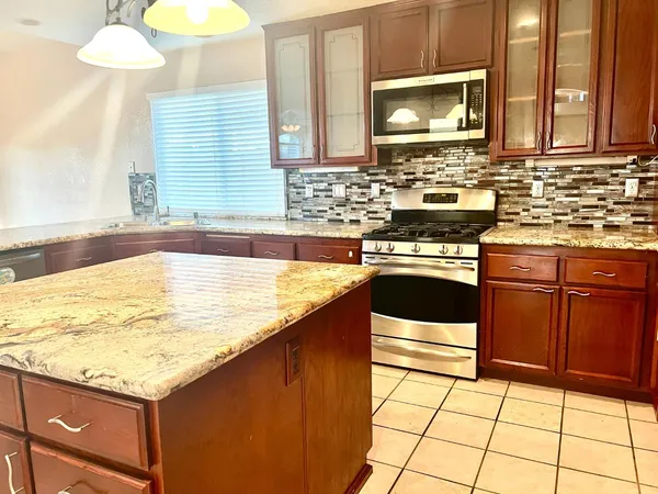 a kitchen with kitchen island granite countertop a stove a sink and a microwave